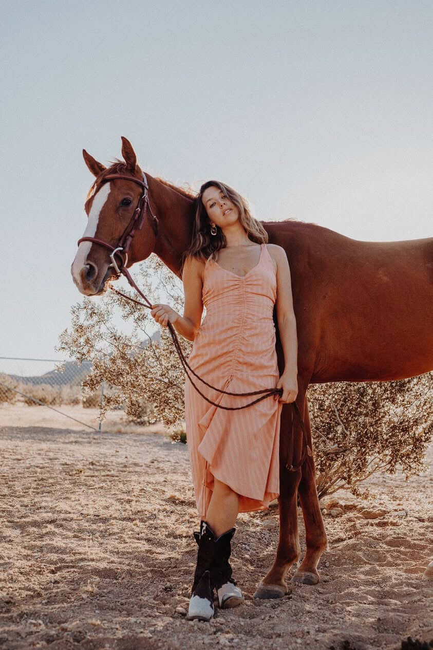 A woman wearing cowboy boots standing with a horse