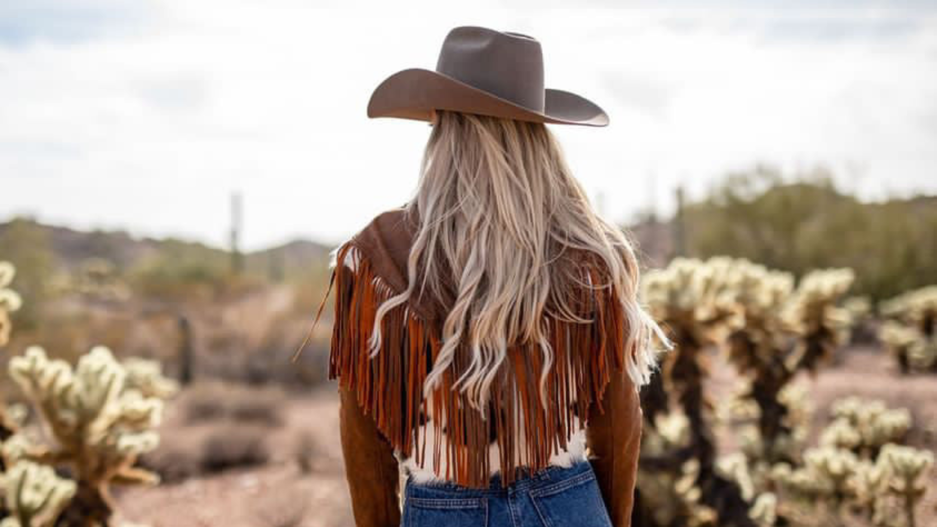 Woman wearing the Charlotte suede & leather cowhide fringe jacket wearing a western hat