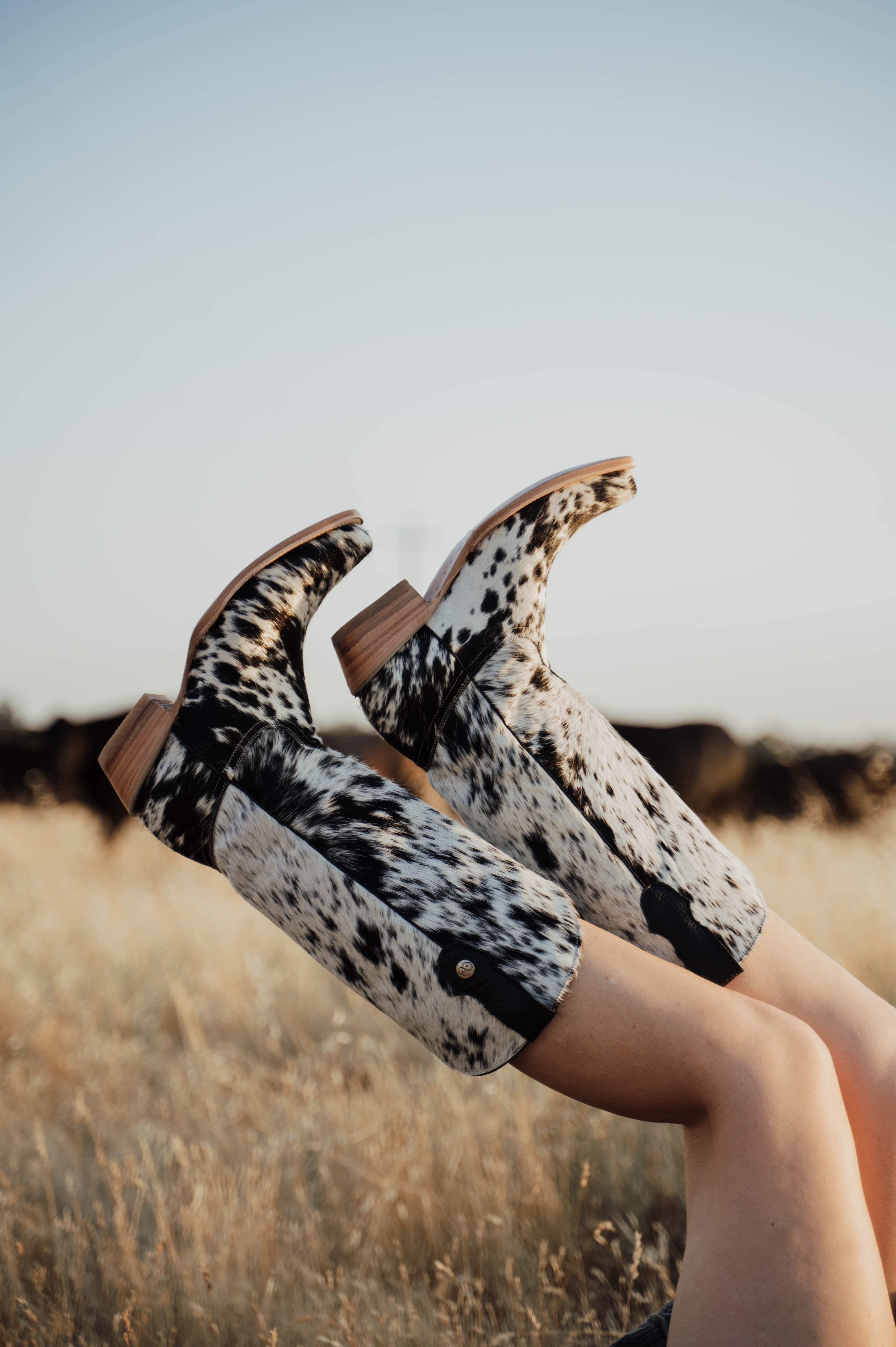 Cow print shoes being worn in a field with a clear sky.